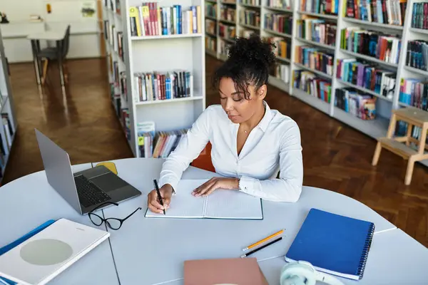 A passionate teacher engages with her students while writing notes in a library packed with books. — Stock Photo