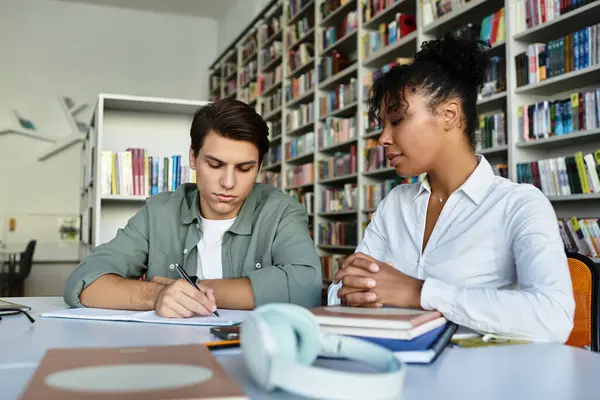 A teacher helps her student focus on writing while surrounded by books and learning materials. — Stock Photo