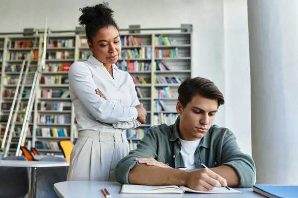 Un mentore guida uno studente mentre si concentra intensamente sui suoi appunti in biblioteca. — Foto stock