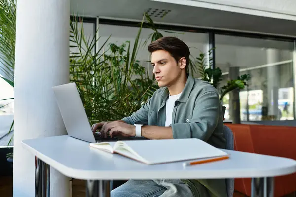 Individuo concentrato si impegna con il suo computer portatile a un tavolo della biblioteca, immerso nel verde. — Foto stock