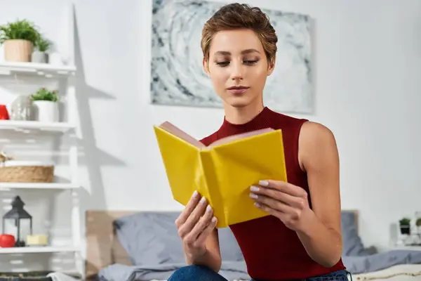 A young woman with short hair relaxes at home, immersed in reading a book in a cozy setting. — Stock Photo