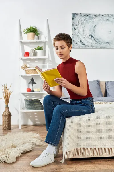Eine junge Frau entspannt zu Hause, in einem Buch versunken, während sie ein rotes Tank-Top und lässige Jeans trägt. — Stockfoto