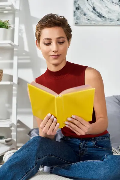 Дома молодая женщина с короткими волосами наслаждается ярко-желтой книгой, наслаждаясь повседневной рутиной.. — стоковое фото