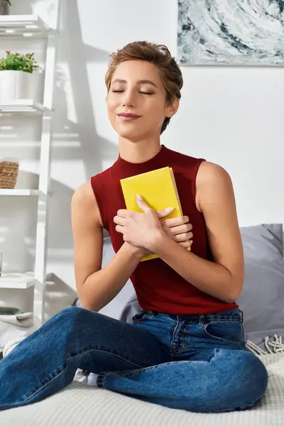 In a relaxed setting, a young woman lovingly embraces a book, lost in her thoughts at home. — Stock Photo