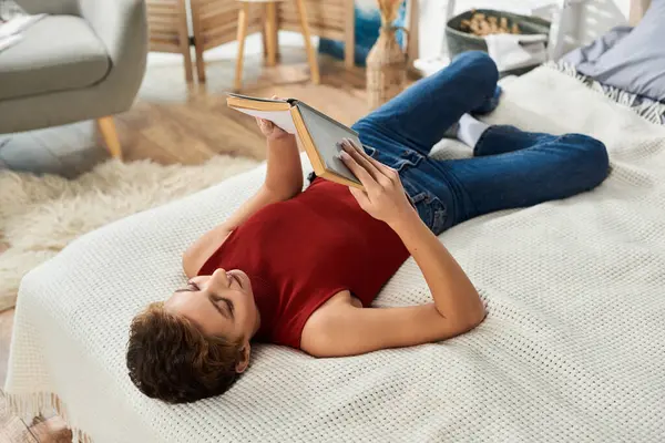 Eine junge Frau entspannt sich auf ihrem Bett, in ein Buch vertieft, während sie ihre ruhige häusliche Umgebung genießt. — Stockfoto