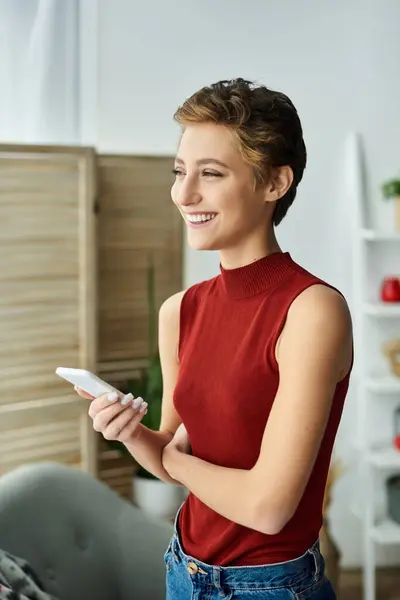 In a cozy home setting, a happy young woman with short hair engages with her phone, enjoying her day. — Stock Photo