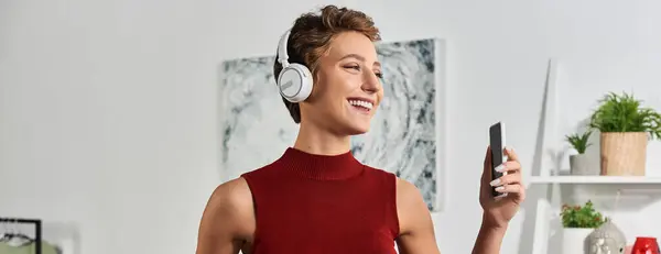 Brilhante e alegre, uma jovem com cabelo curto relaxa em sua casa enquanto ouve música. — Fotografia de Stock