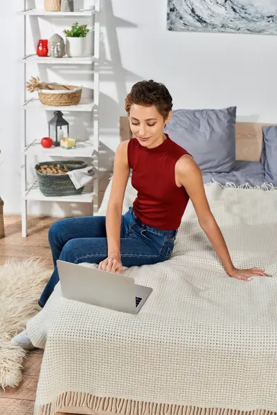 Una giovane donna con i capelli corti si impegna nella sua routine quotidiana, lavorando sul suo computer portatile in un ambiente domestico accogliente. — Foto stock