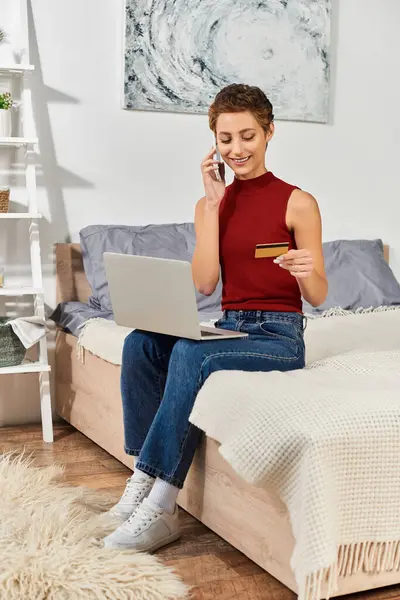 Em um espaço acolhedor, uma jovem se envolve em compras on-line, equilibrando seu telefonema enquanto sorri. — Fotografia de Stock