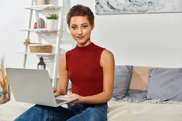 Uma jovem com cabelo curto se engaja com seu laptop enquanto relaxa em casa em um ambiente acolhedor. — Fotografia de Stock