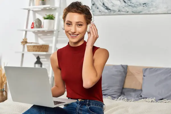 Una giovane donna con i capelli corti e il trucco naturale sorride mentre usa il suo computer portatile a casa in un'atmosfera rilassata. — Foto stock