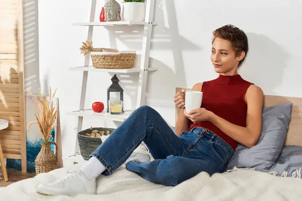 A young woman in a red tank top savors her warm beverage, embracing a peaceful morning routine at home. — Stock Photo
