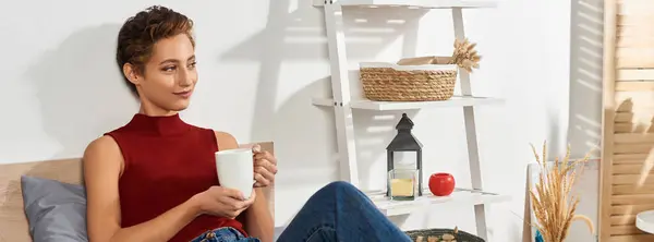A young woman with short hair relaxes at home, sipping tea while embracing her daily routine in comfort. — Stock Photo