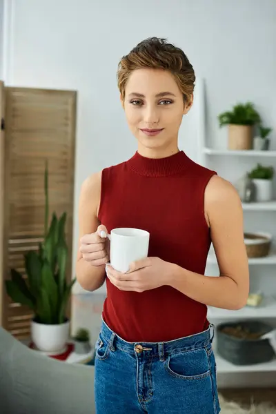 Uma jovem alegre com cabelo curto saboreia seu café da manhã enquanto relaxa em casa, abraçando a vida diária. — Fotografia de Stock