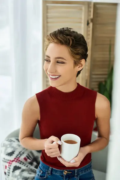 Bright and radiant, a young woman in a red tank top savors her tea at home, embracing the moment. — Stock Photo
