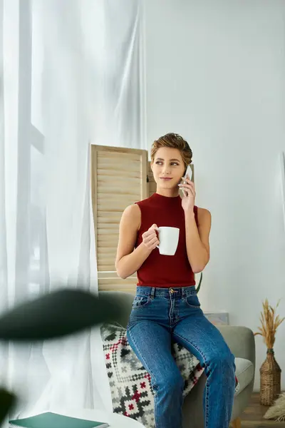 The young woman sits comfortably, talking on the phone and sipping her coffee, embracing a relaxed morning. — Stock Photo