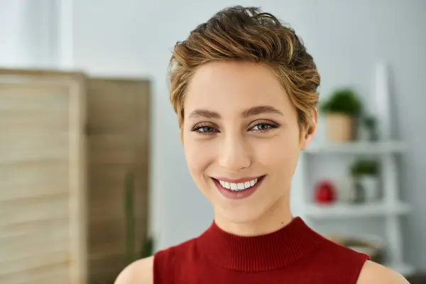 A young woman with short hair smiles radiantly in her red tank top, enjoying a relaxed day at home. — Stock Photo