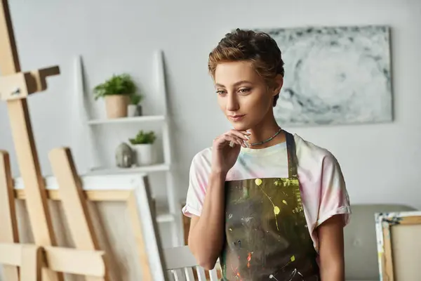 Uma jovem mulher com uma expressão pensativa se envolve na pintura, cercada por seus suprimentos de arte e criatividade. — Fotografia de Stock