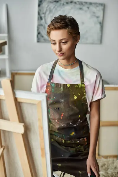 Una joven con el pelo corto se dedica alegremente a pintar en casa, sumergiéndose en su pasatiempo creativo. - foto de stock
