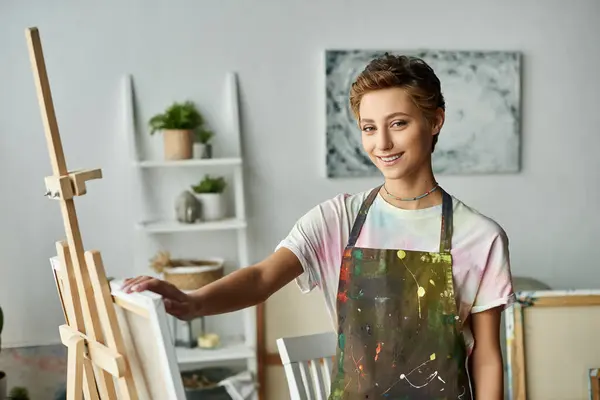 A young woman with natural makeup and short hair joyfully paints at her creative home studio. — Stock Photo