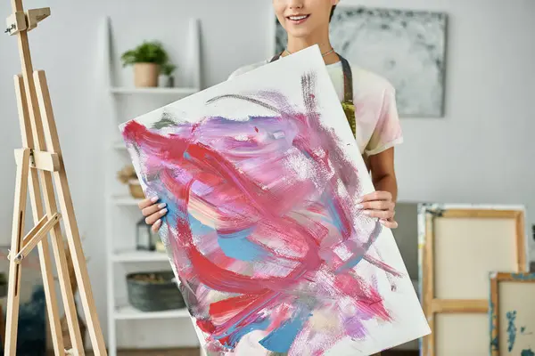 En un ambiente acogedor en casa, una joven con el pelo corto muestra su pintura abstracta vibrante. - foto de stock
