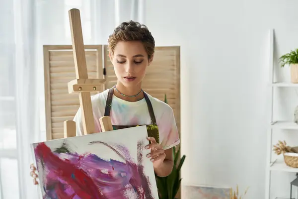 A young woman with natural makeup paints vibrant artwork in her cozy home studio, expressing her creativity. — Stock Photo