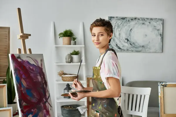 In a cheerful home studio, a young woman with short hair enjoys painting, surrounded by creativity and color. — Stock Photo