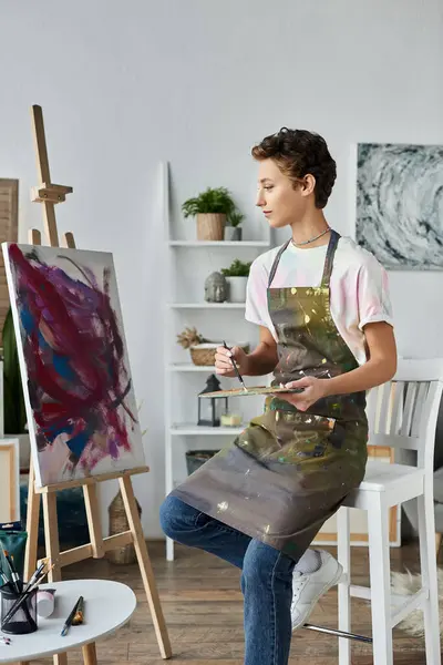 A young woman in an apron paints a colorful picture, fully immersed in her artistic hobby at home. — Stock Photo