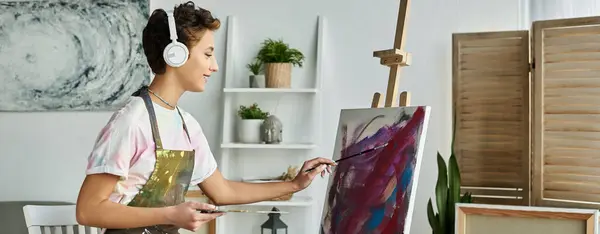 Una joven inmersa en la pintura en casa, con auriculares y rodeada de sus materiales artísticos. - foto de stock