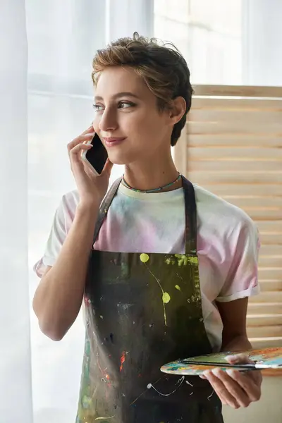 Una joven está disfrutando de su pasatiempo artístico, pintando en casa mientras charla por teléfono. - foto de stock
