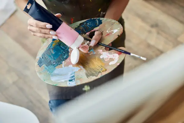 Una joven con maquillaje natural se sumerge en la pintura en casa, expresando su lado artístico. - foto de stock