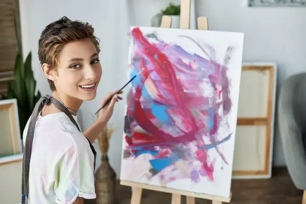 A young woman with natural makeup enjoys painting on canvas, expressing her artistic side in her cozy home. — Stock Photo