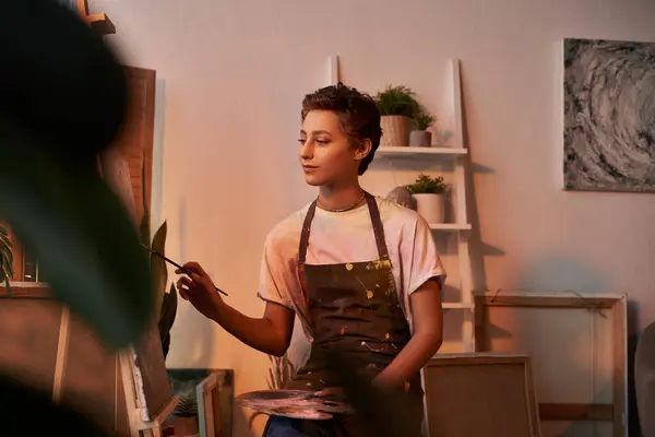 A young woman with natural makeup and short hair passionately paints at home, immersing herself in art. — Stock Photo