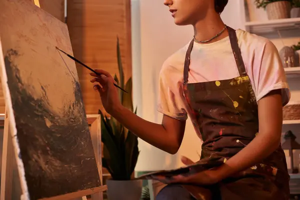 A young woman expresses her creativity by painting a canvas in her home, surrounded by a tranquil atmosphere. — Stock Photo