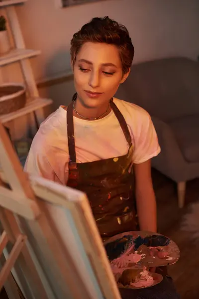 Una joven disfruta pintando sobre lienzo en su acogedora casa, abrazando su lado artístico con una suave iluminación. - foto de stock