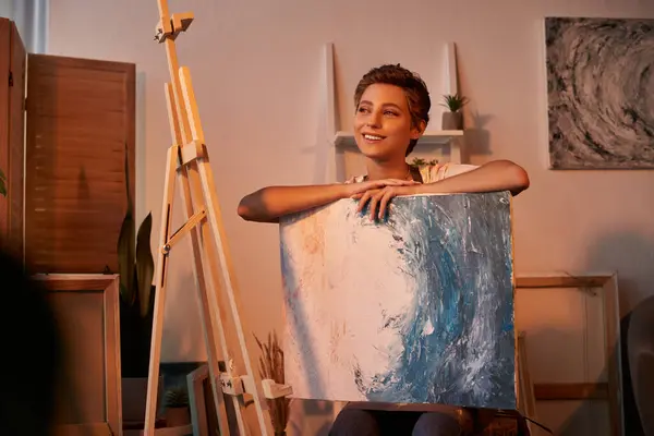 A la maison, une jeune femme au maquillage naturel peint joyeusement sur toile, immergée dans son passe-temps créatif. — Photo de stock