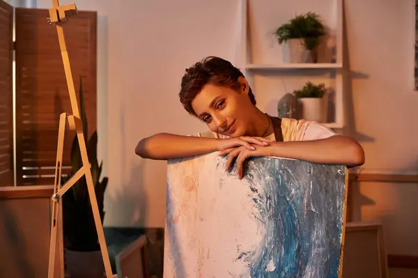 En un acogedor entorno hogareño, una joven con maquillaje natural se sumerge en la pintura, expresando creatividad. - foto de stock