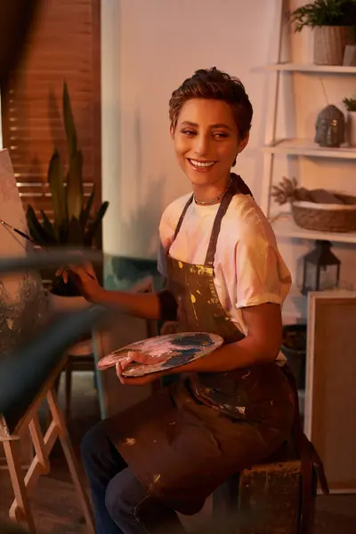 Una joven con maquillaje natural pinta felizmente en casa, abrazando su afición creativa en un ambiente cálido. - foto de stock