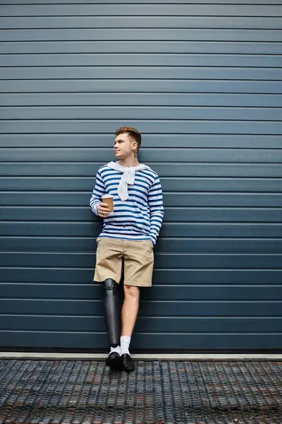 The young man stands confidently with a coffee cup, showcasing his prosthetic leg. — Stock Photo