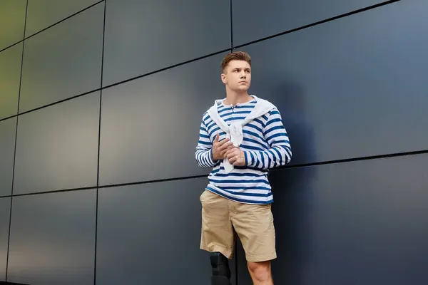 A young man wearing a striped shirt leans against a sleek wall, exuding determination and style. — Stock Photo