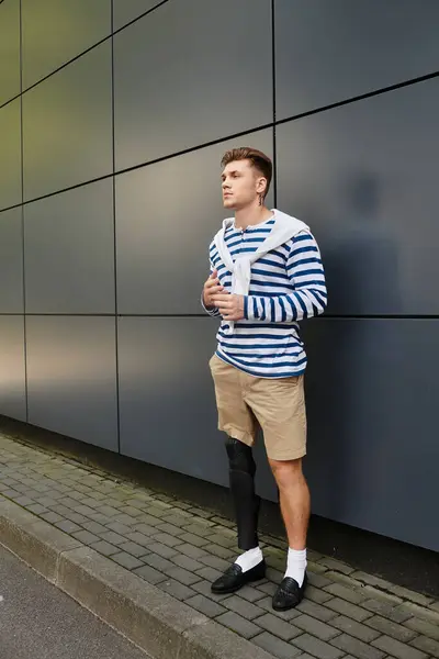 A stylish young man in a striped shirt stands confidently outdoors, highlighting his prosthetic leg. — Stock Photo