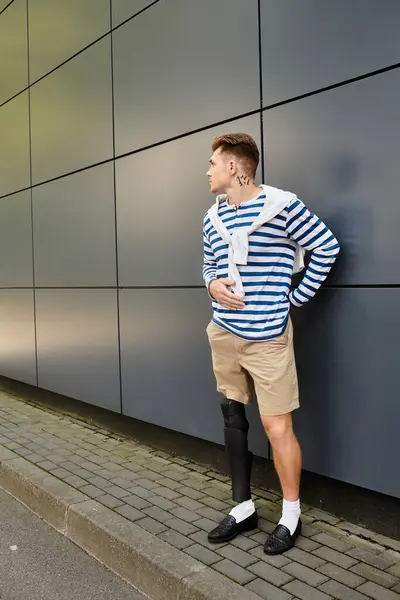 A stylish young man stands confidently against a sleek building, showcasing his prosthetic leg. — Stock Photo