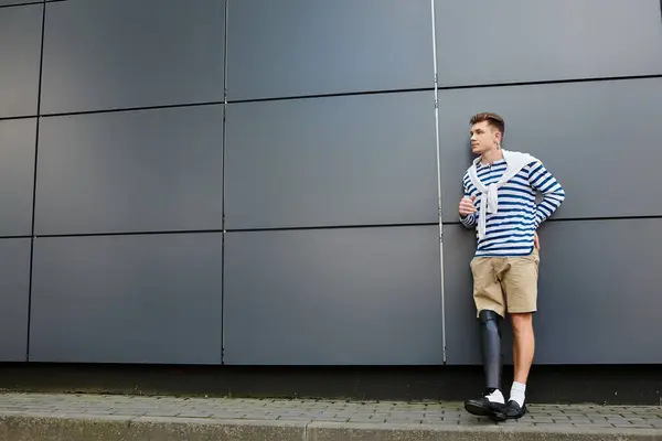 Un joven se apoya contra una pared, mostrando orgullosamente su pierna protésica a la luz del día. - foto de stock