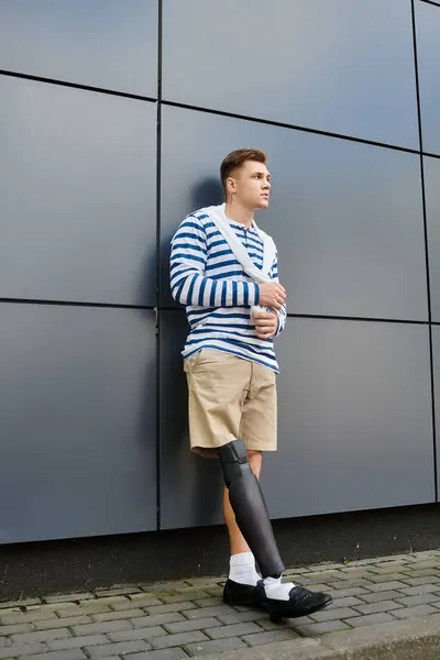 A handsome young man stands confidently at a contemporary building, showcasing his prosthetic leg. — Stock Photo