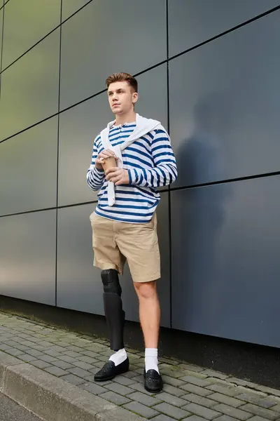El joven se apoya en un edificio elegante, sosteniendo una bebida y exudando confianza. — Stock Photo