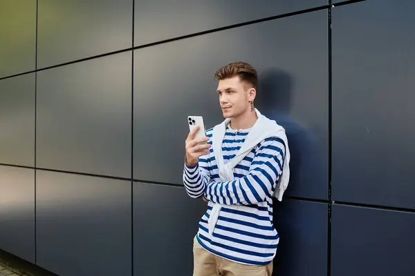 Un joven con una pierna protésica se para casualmente, sosteniendo un teléfono inteligente en un entorno moderno. - foto de stock