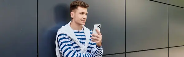 A stylish young man with a prosthetic leg leans against a sleek wall, absorbed in his phone. — Stock Photo