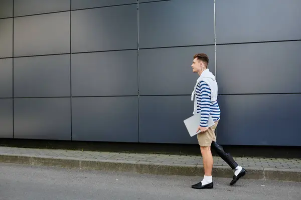 A young man strides confidently along a modern urban pathway, laptop in hand. — Stock Photo