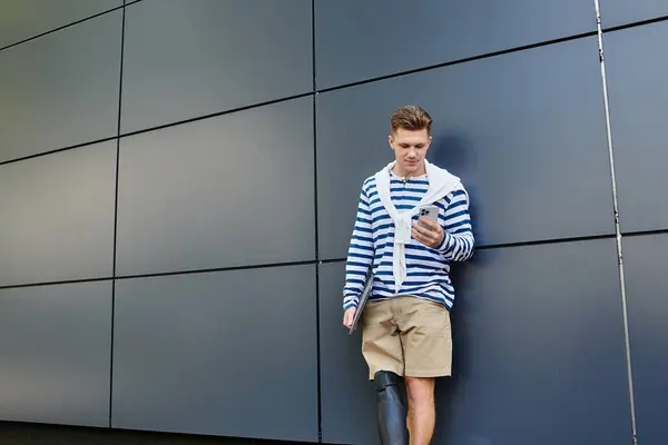 A stylish young man with a prosthetic leg takes a break, engrossed in his phone outside. — Stock Photo