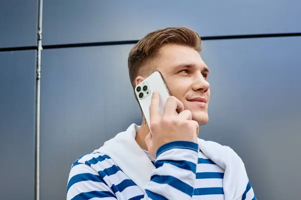 Молодий чоловік посміхається, розмовляючи на своєму смартфоні на фоні сучасної будівлі. — стокове фото